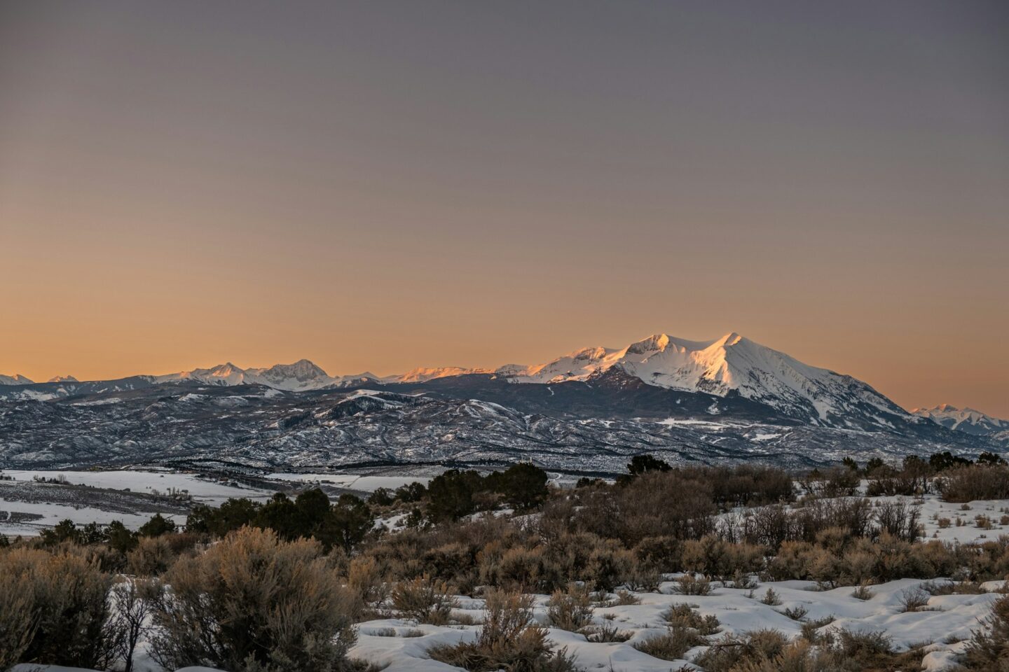 Mount Sopris at sunset, its twin summits lit orange above sagebrush and juniper on a high mesa.